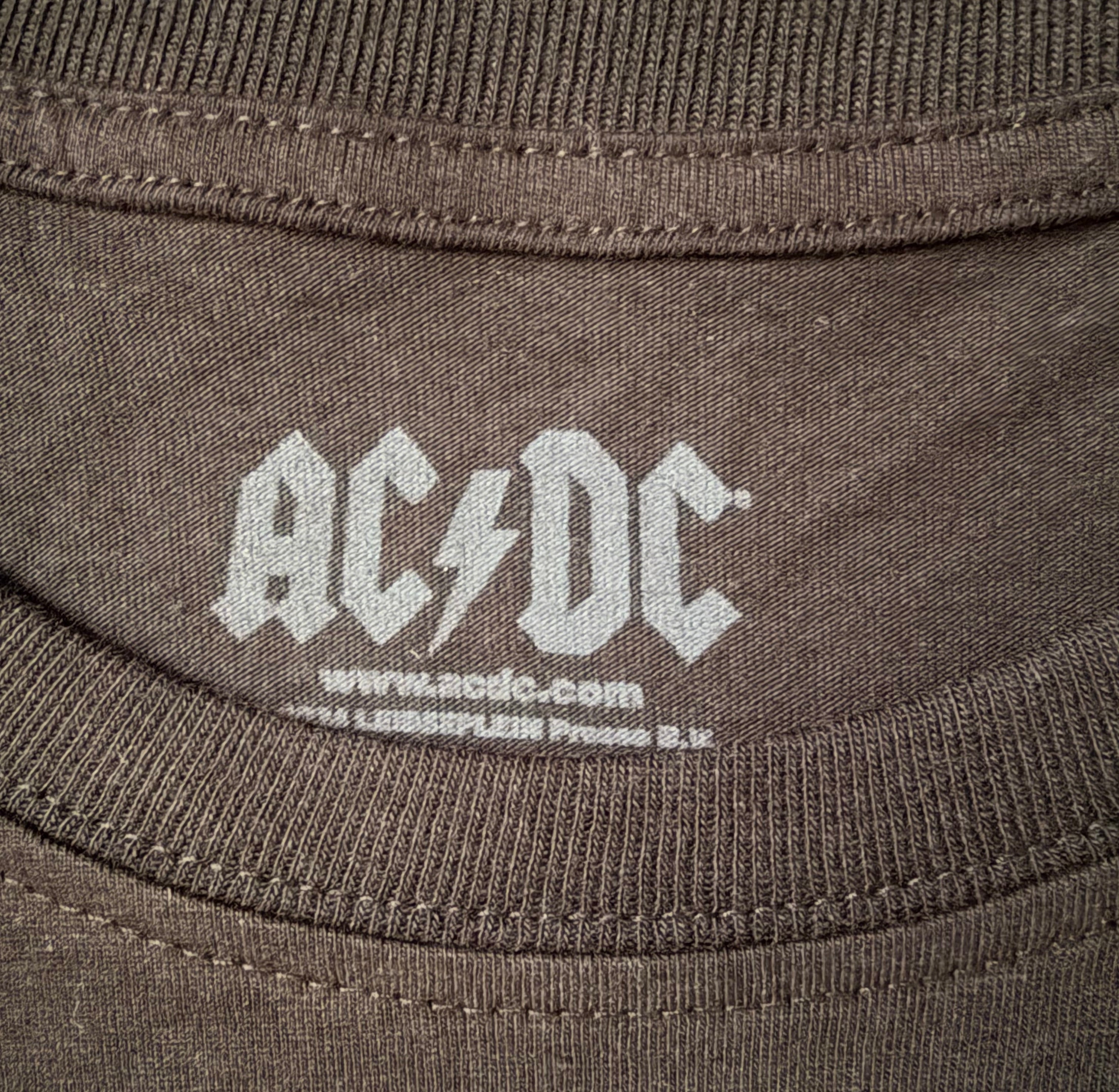 Close-up detail of the inner neck collar of the official black AC/DC graphic t-shirt, showing the white screen-printed band logo and merchandise information.