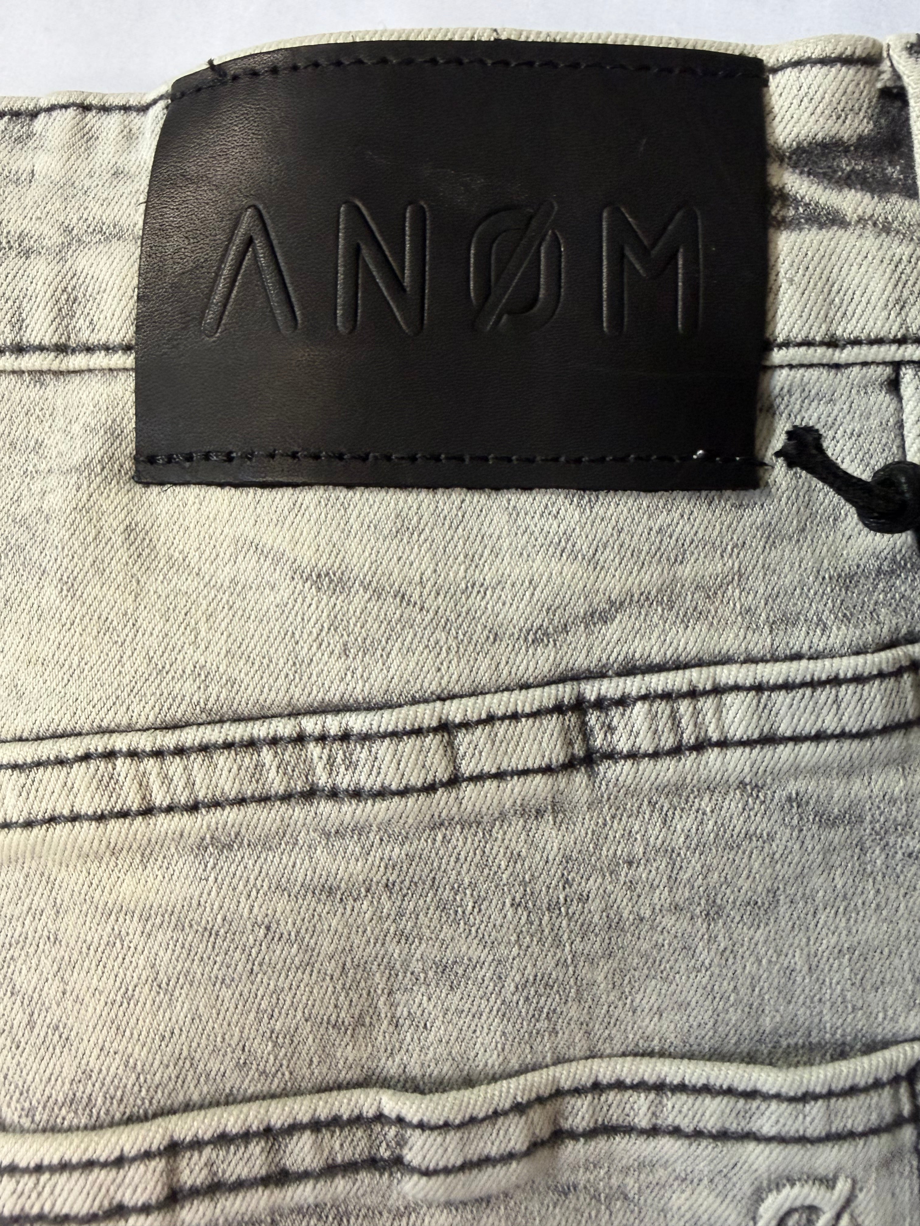 Macro detail view of a premium black leather waistband patch on AMNÉ modern streetwear denim jeans. Features a debossed geometric brand logo over a heavily textured grey acid wash canvas.
