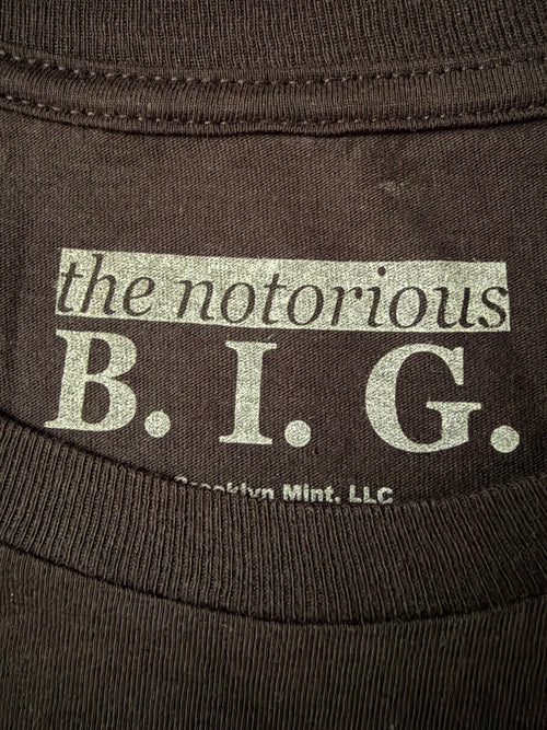 Close-up of the screen-printed inside neck collar of the official black Notorious B.I.G. unisex t-shirt, showing the white brand logo text and Brooklyn Mint licensing info.