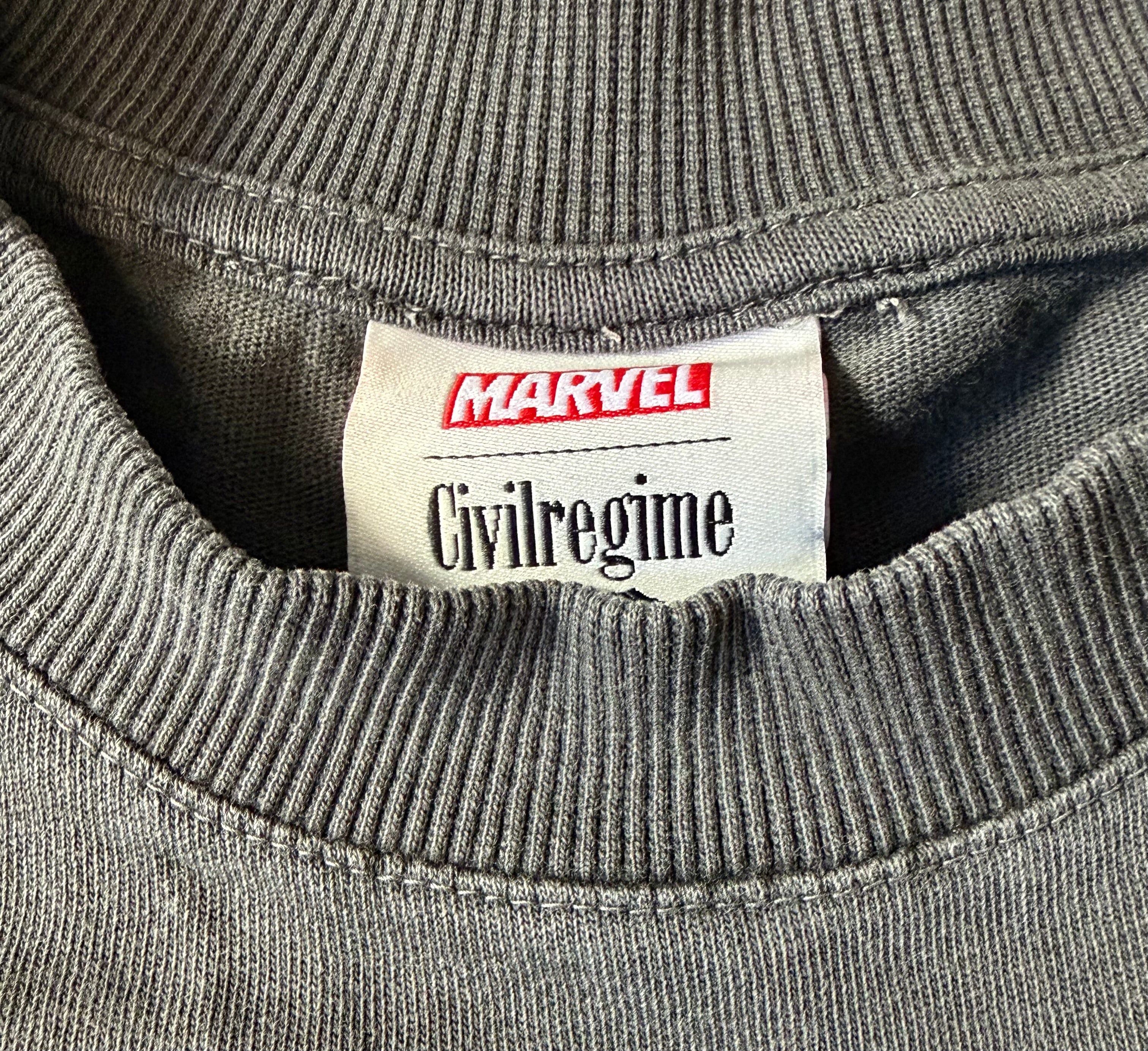 Close-up of a gray ribbed knit garment neck label reading Marvel and Civilregime.