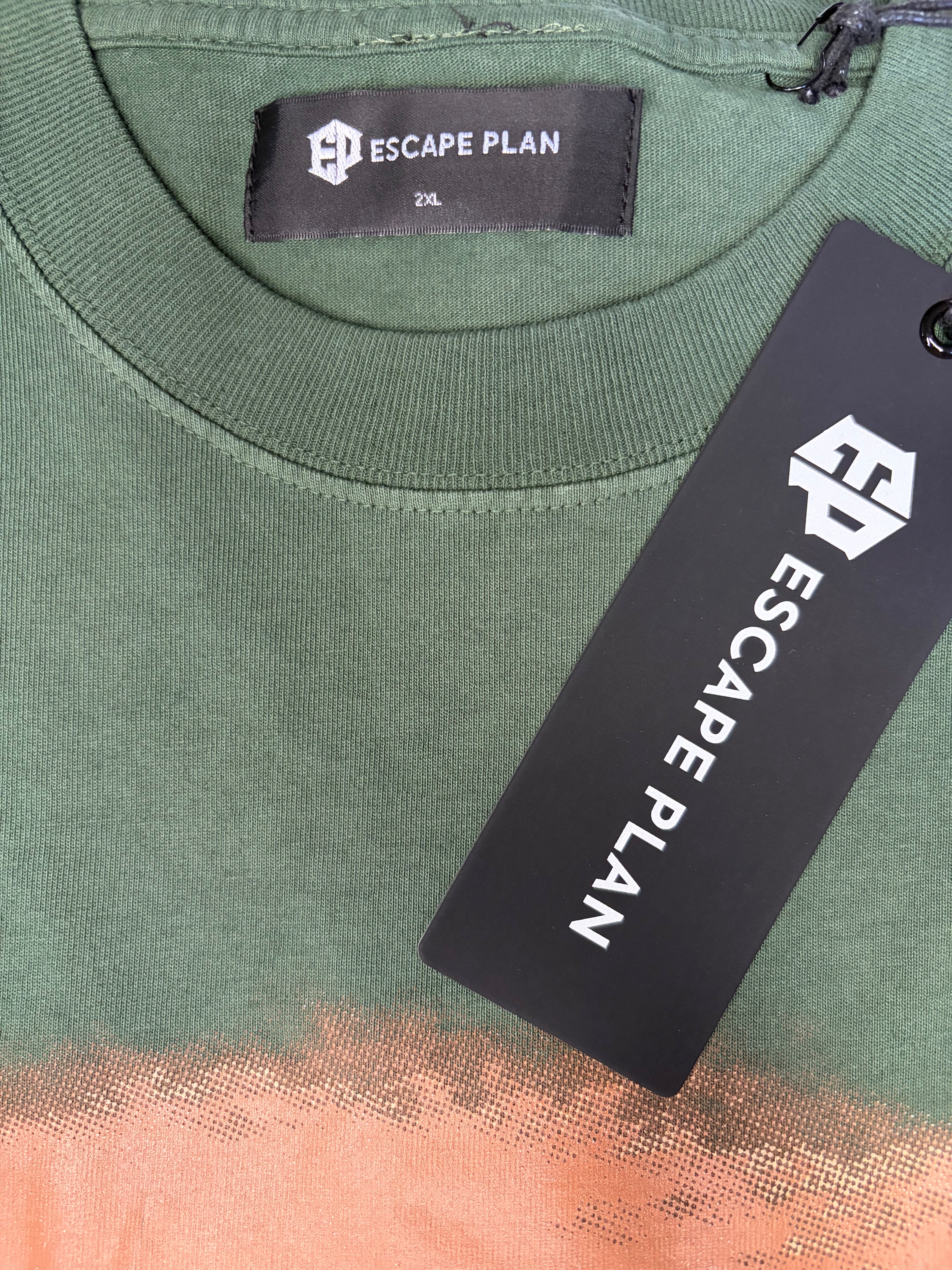 Close-up of an Escape Plan t-shirt in olive green with a peach-colored halftone pattern at the bottom, featuring a black neck label and a black product tag.