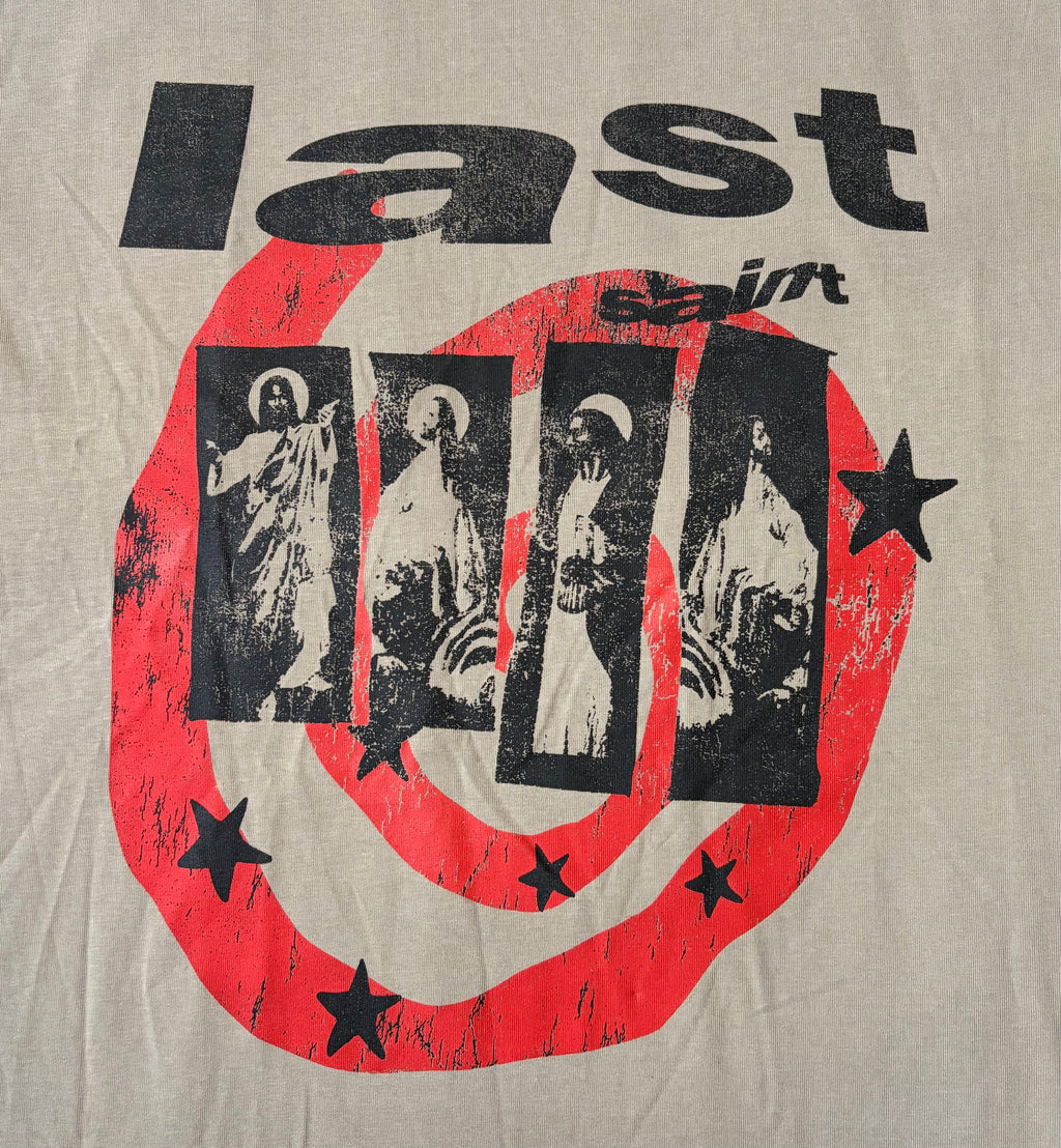A close-up of a beige graphic print featuring the word 'last' in distressed black lettering above a large red circular design with black stars and four vertical black panels containing religious figures.
