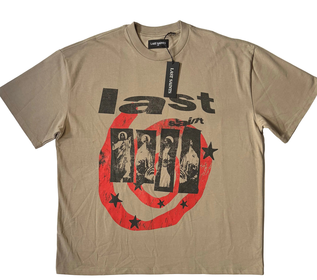 A beige Last Saints short sleeve graphic T-shirt featuring bold black typography that reads "last saint" layered over a four-panel religious portrait artwork. The graphic includes a large, distressed red circular swirl pattern decorated with black stars across the front. A black brand hang tag is attached to the collar line.