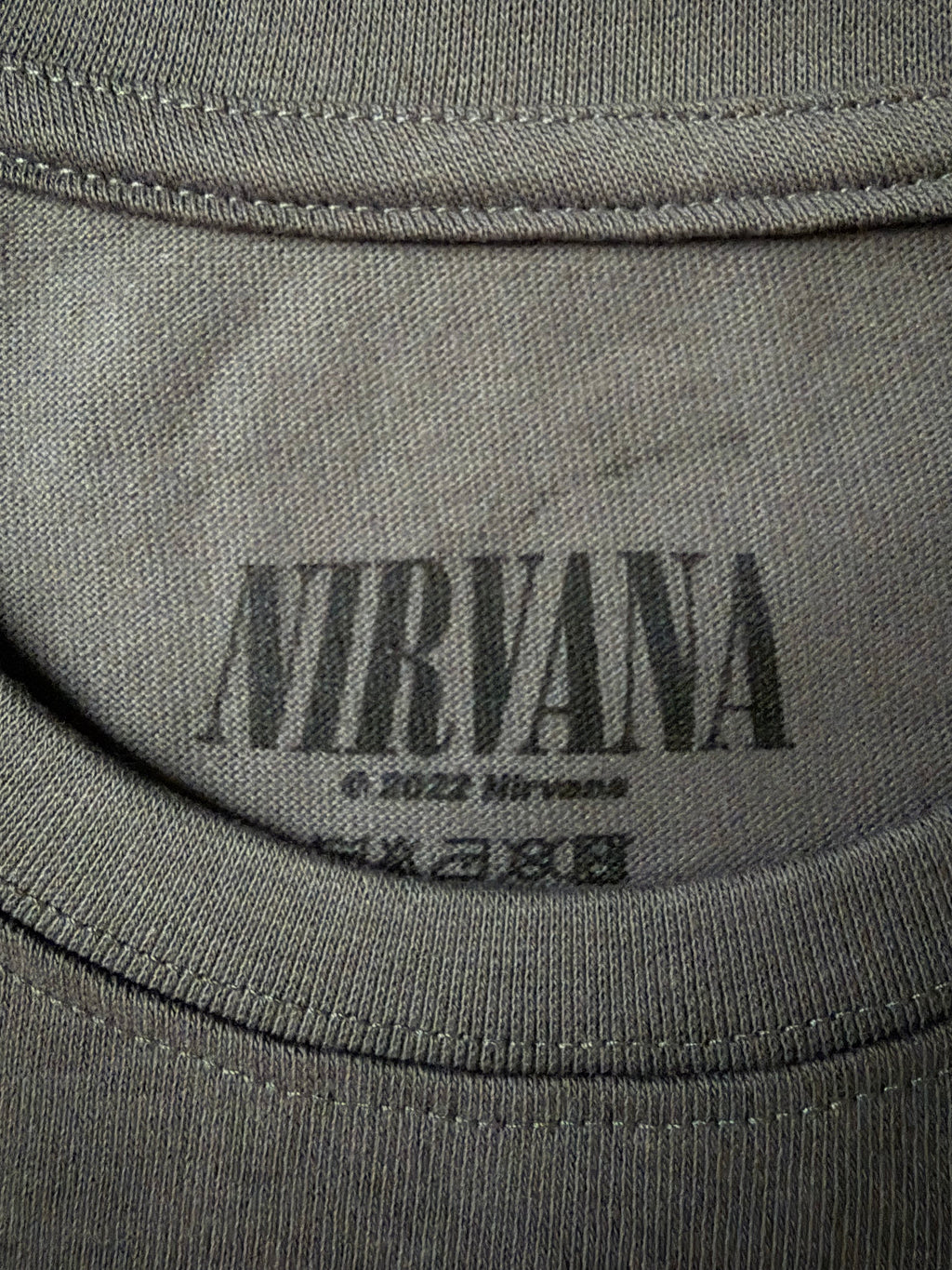 Close-up of the screen-printed inside neck collar of the official charcoal grey Nirvana unisex t-shirt, showing the black distressed logo and copyright text.