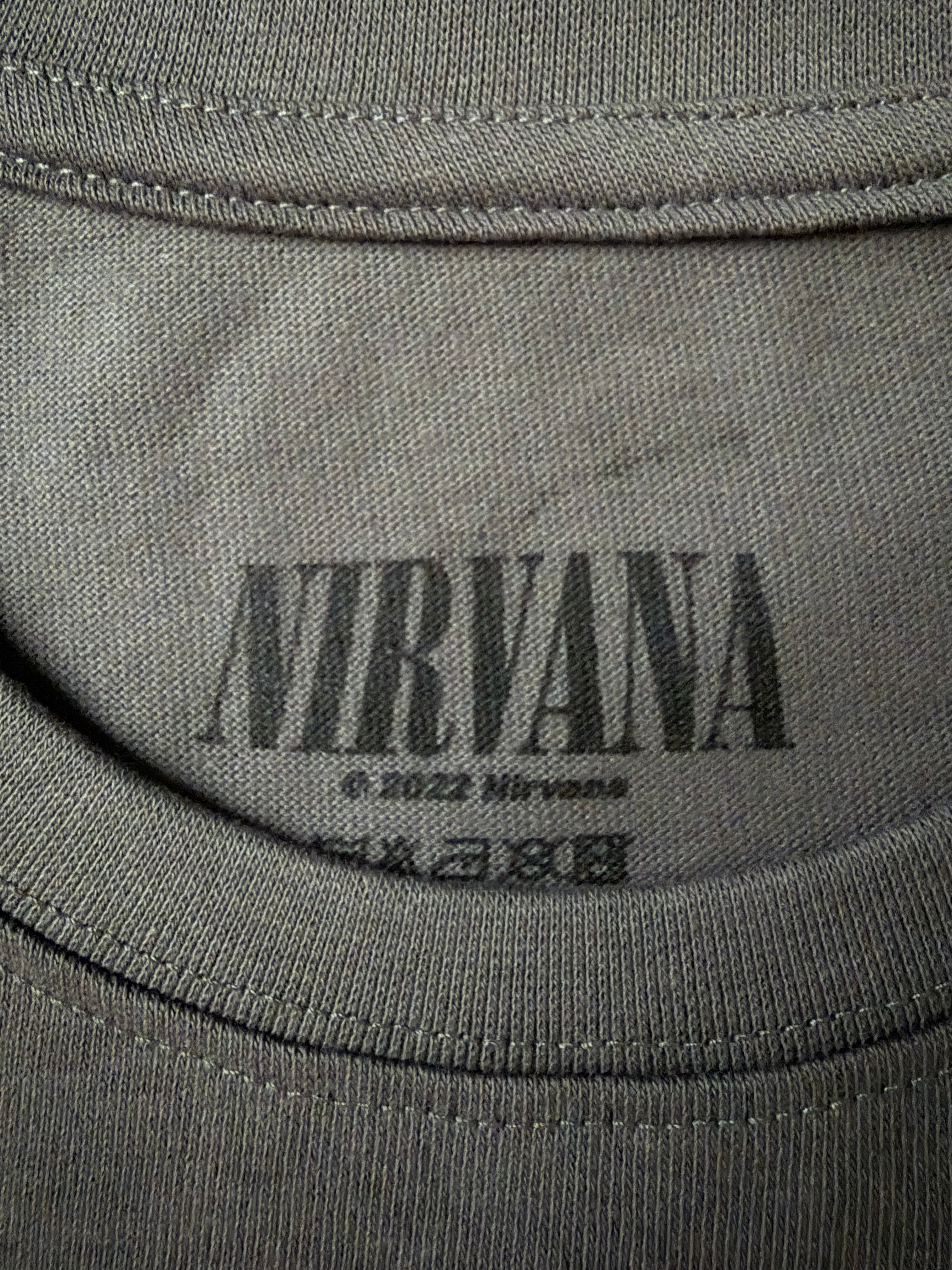 Close-up of the screen-printed inside neck collar of the official charcoal grey Nirvana unisex t-shirt, showing the black distressed logo and copyright text.