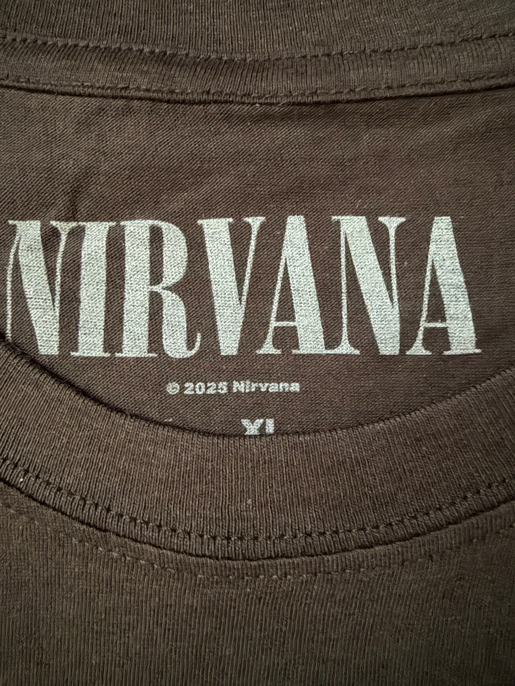 Close-up of the screen-printed inside neck collar of the official black Nirvana unisex t-shirt, showing the white distressed band logo and copyright branding detail.