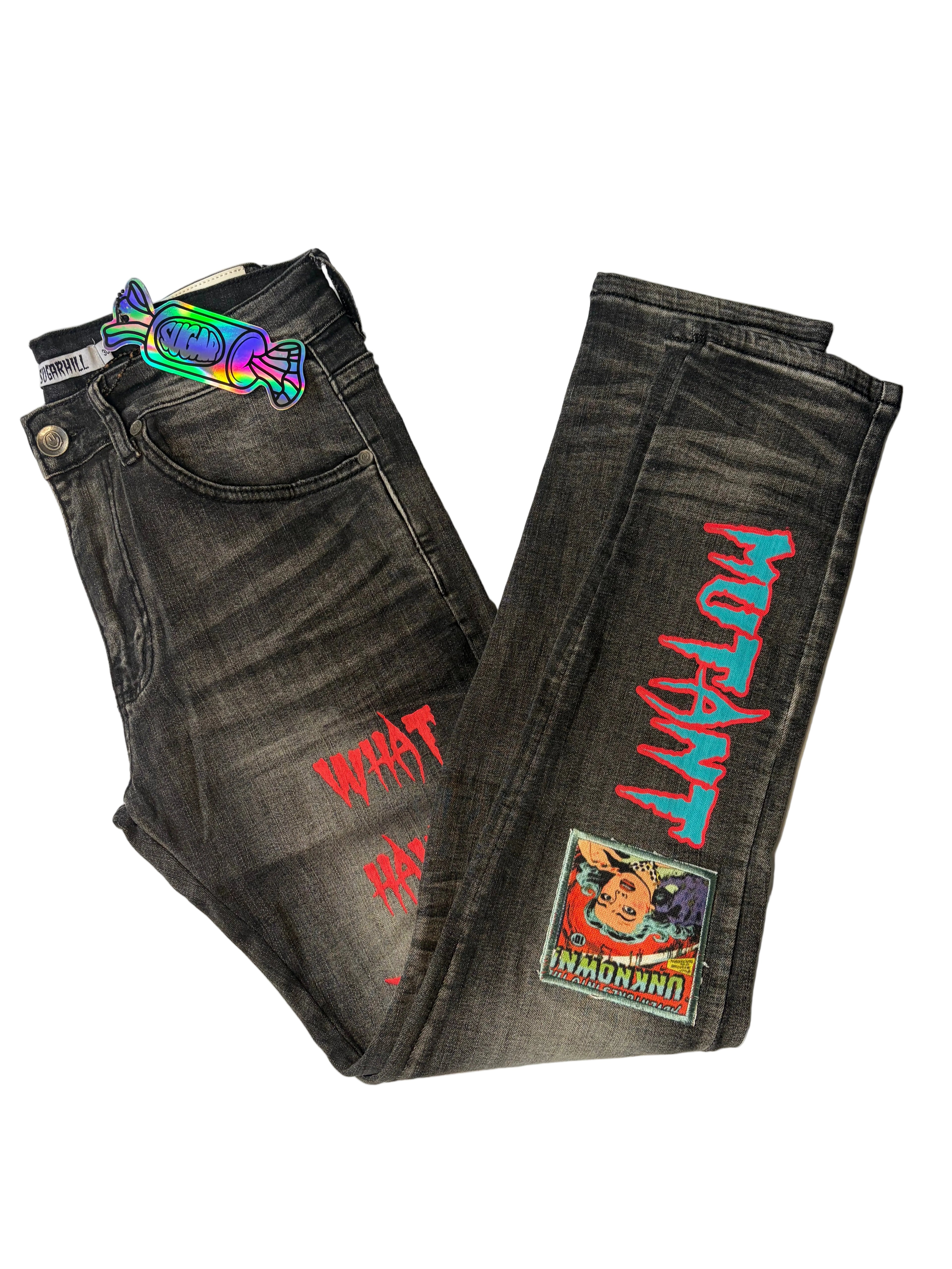Alternate side view of Sugarhill modern streetwear graphic jeans in washed black charcoal denim. Features bright turquoise and pink "MUTANT" embroidery, an illustrated comic-book art patch, and a holographic candy logo tag.
