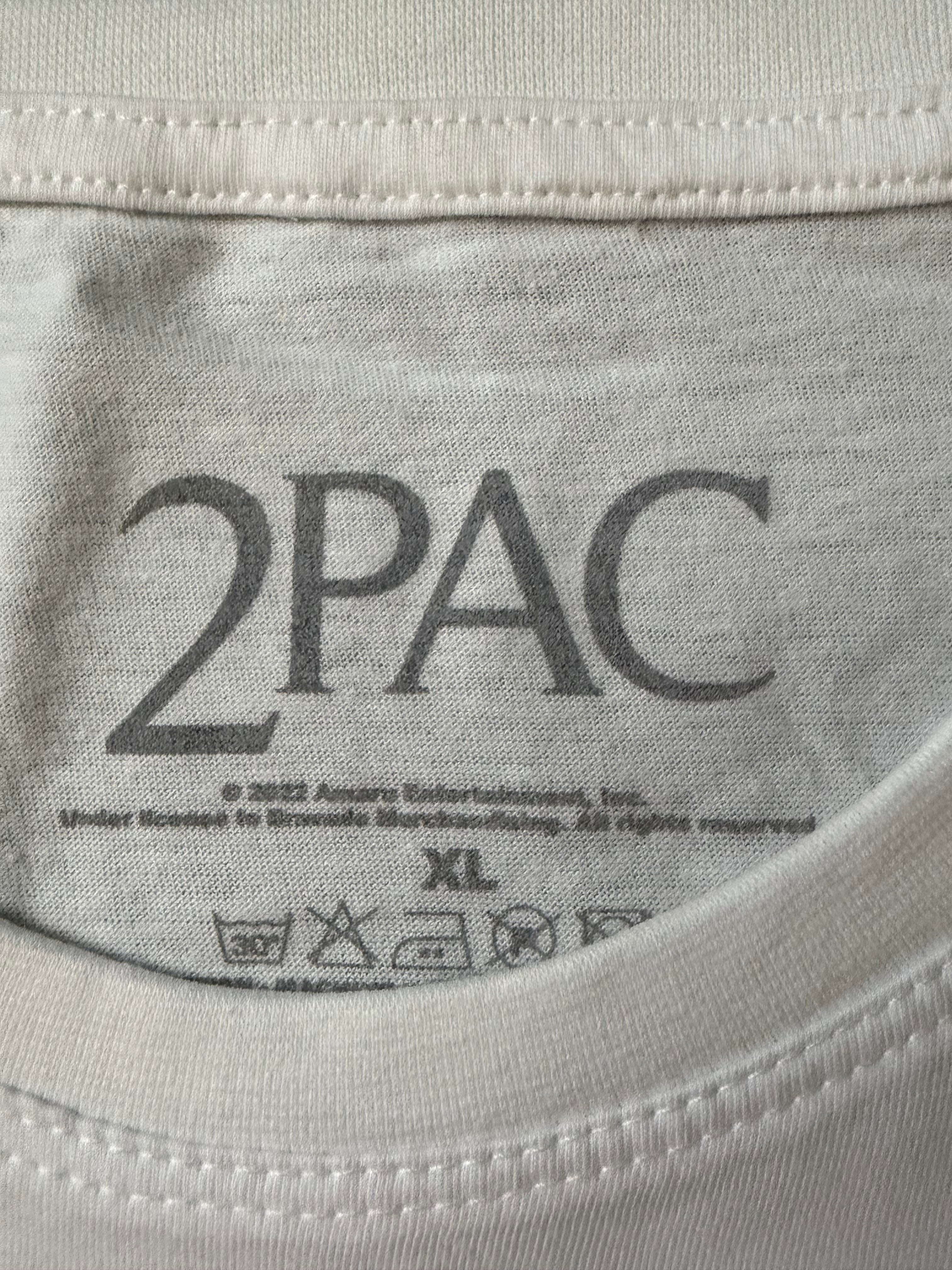 Close-up of the screen-printed inside neck collar of the official white Tupac unisex t-shirt, showing the dark gray 2Pac branding logo, size XL, and care instructions.